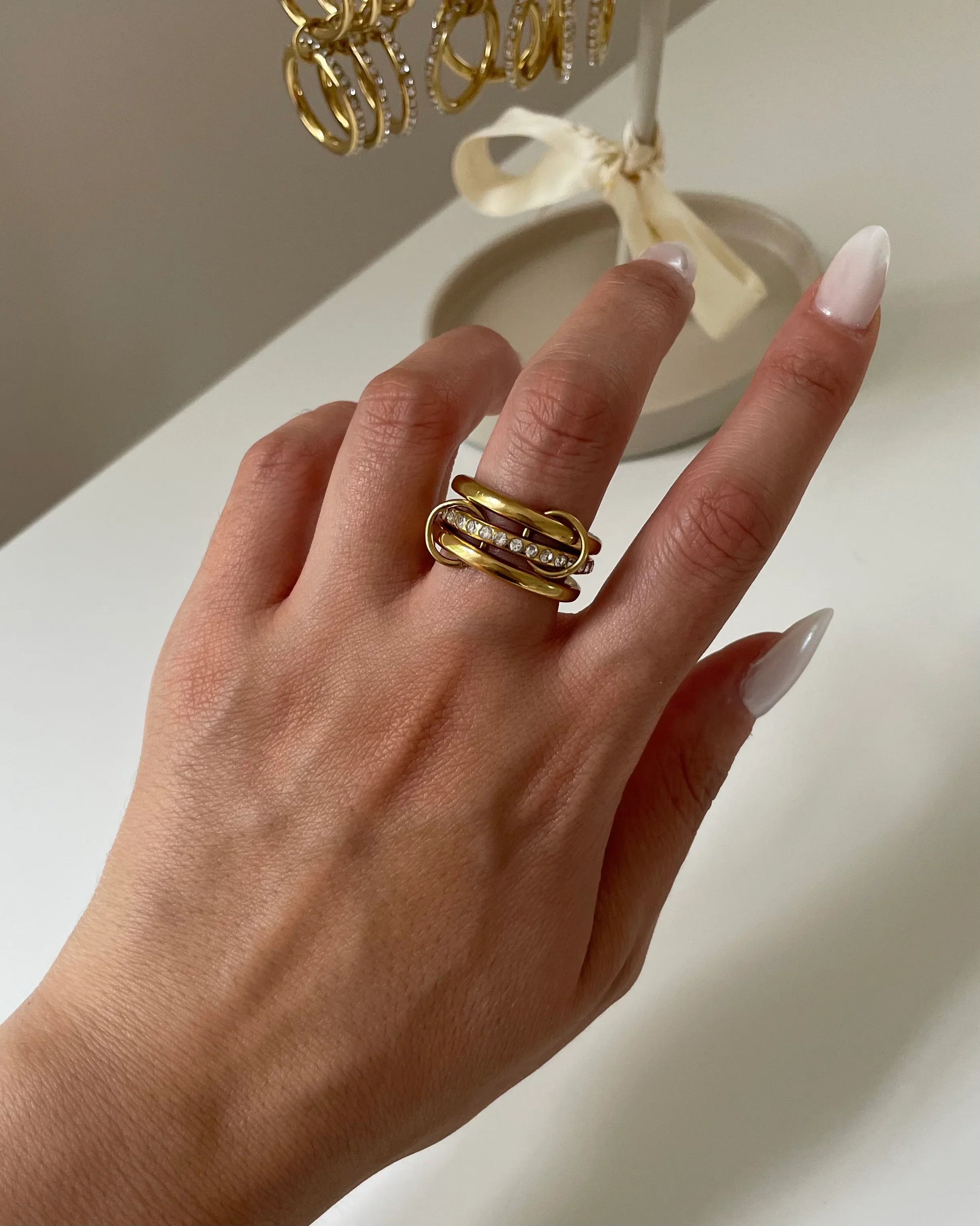 Hand mit elegantem goldfarbenem Ring mit Kristallen und französischer Maniküre auf weißem Tisch