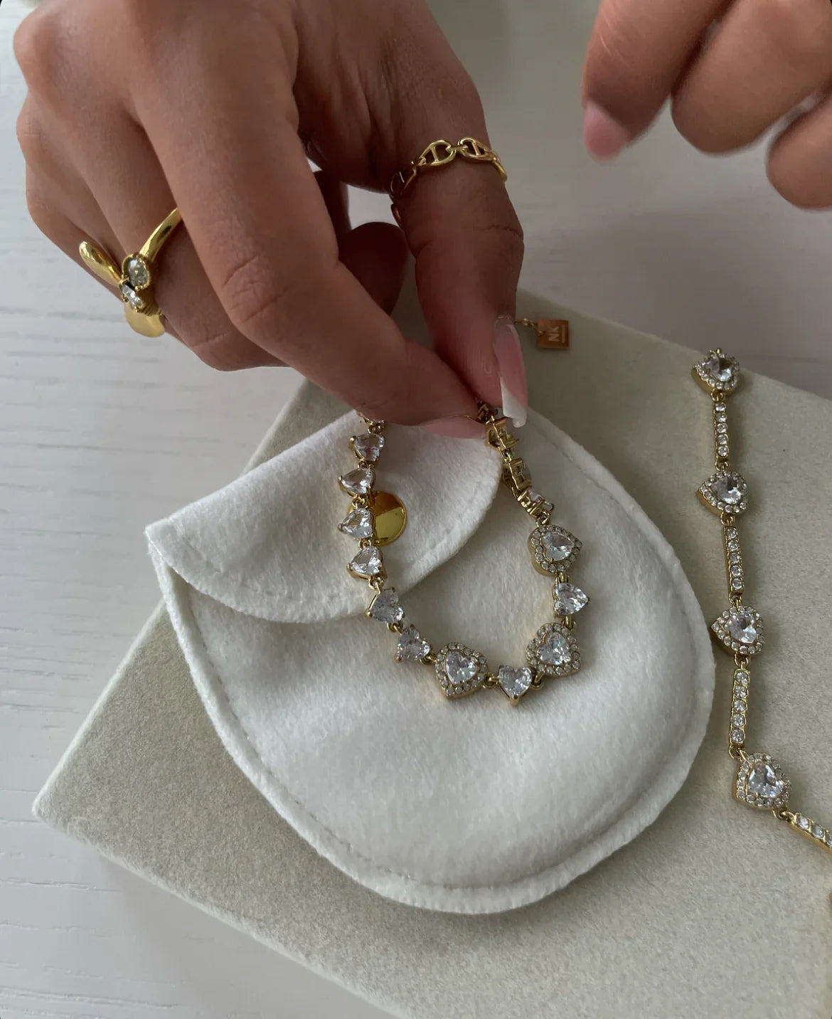 Hand mit goldenen Ringen hält Herzklare Kristallarmbänder auf weißem Filzetui