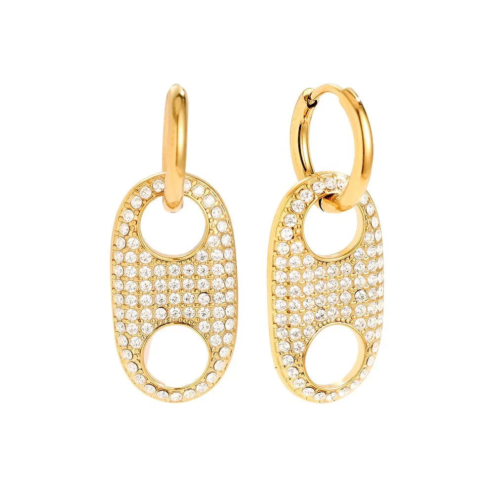 Goldene Ohrringe mit ovalen Anhängern und strassbesetzten Details auf weißem Hintergrund
