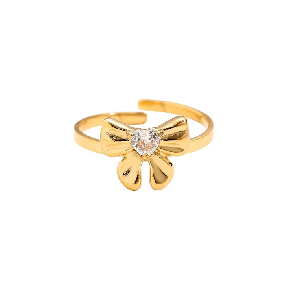 Goldener Ring mit Schleifen-Design und herzförmigem Kristall auf weißem Hintergrund