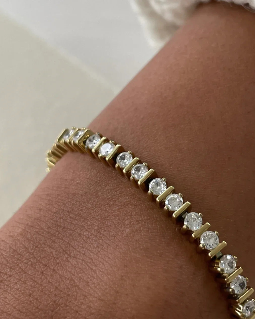 Nahaufnahme eines goldenen Tennisarmbands mit klaren Diamanten an einem hellbraunen Handgelenk