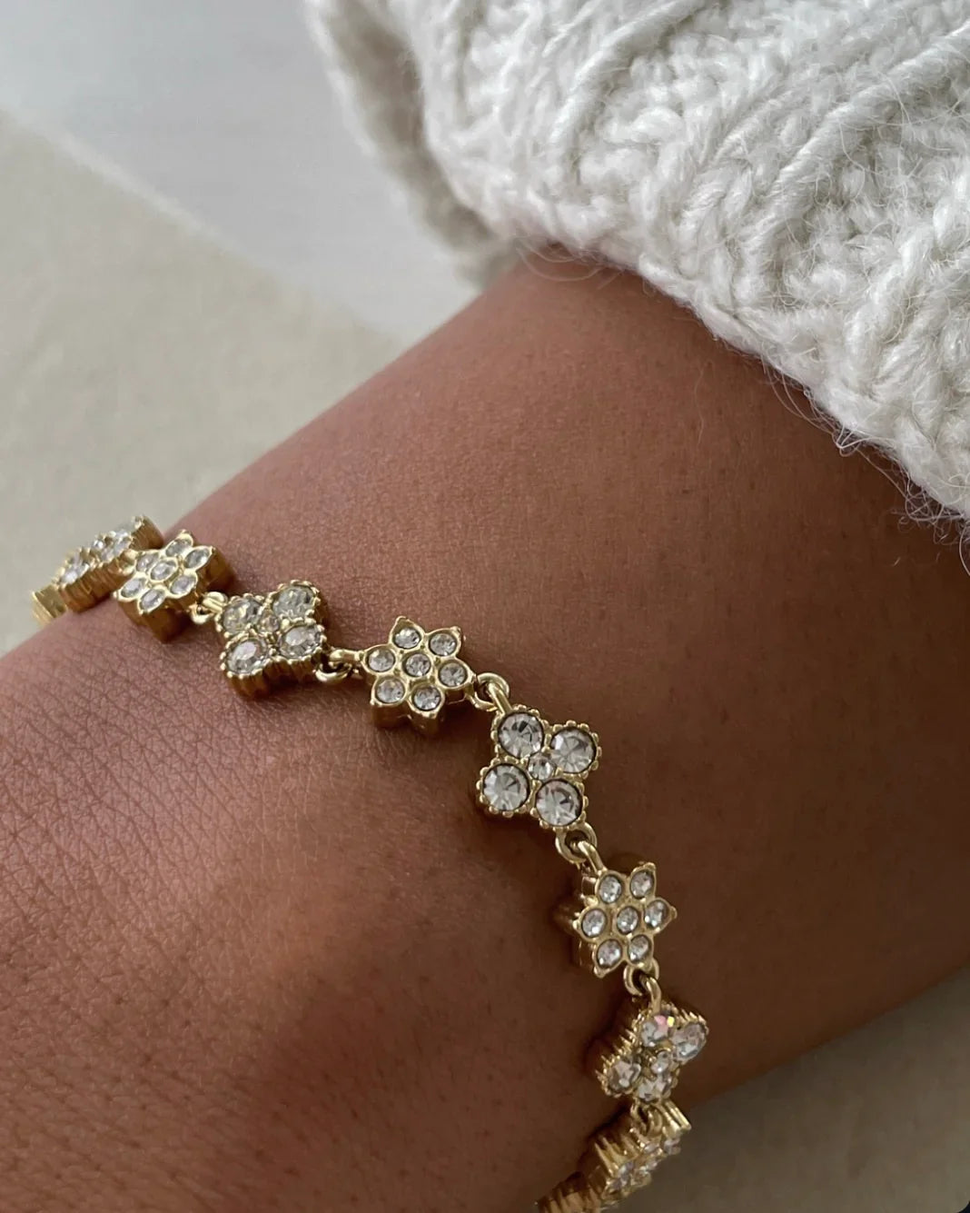 Goldfarbenes Armband mit klaren Kristallblumen an Handgelenk mit cremeweißem Strickpullover