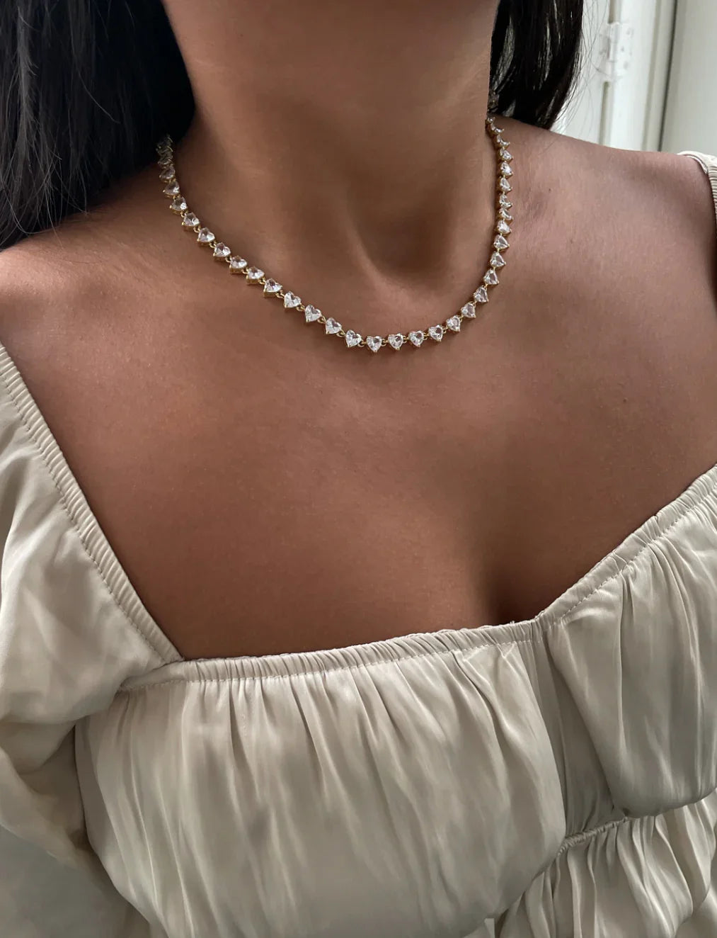 Frau trägt goldene Halskette mit herzförmigen Diamanten zu weißem Satin-Oberteil