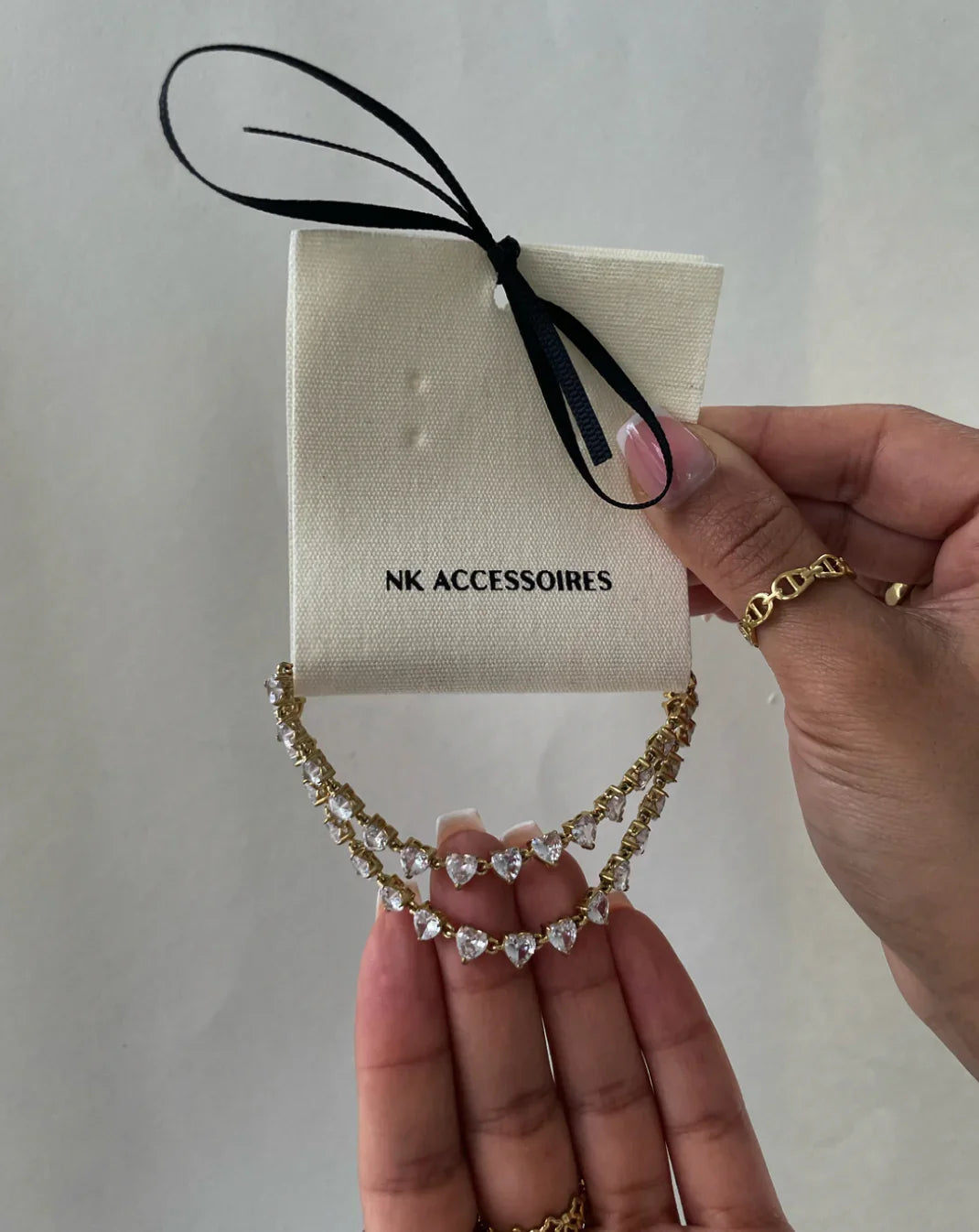 Goldene Halskette mit herzförmigen Kristallen, gehalten an NK Accessoires Karte mit schwarzer Schleife