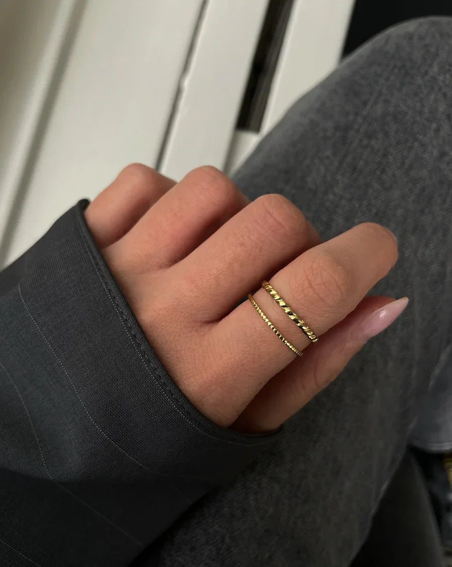 Hand mit zwei filigranen goldenen Ringen auf weißem und grauem Hintergrund, modische Nahaufnahme