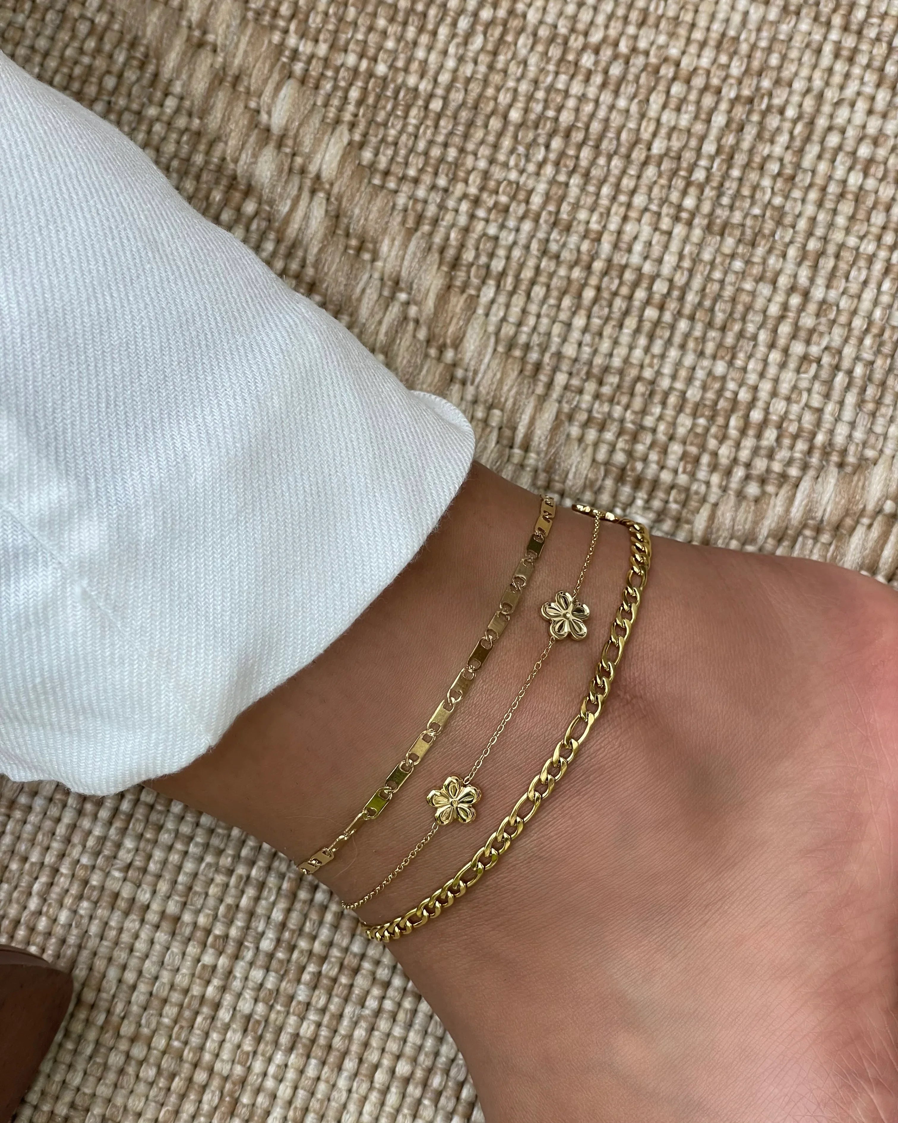 Frau trägt drei goldene Fußketten mit Blumen- und Gliederdesign auf Strukturteppich