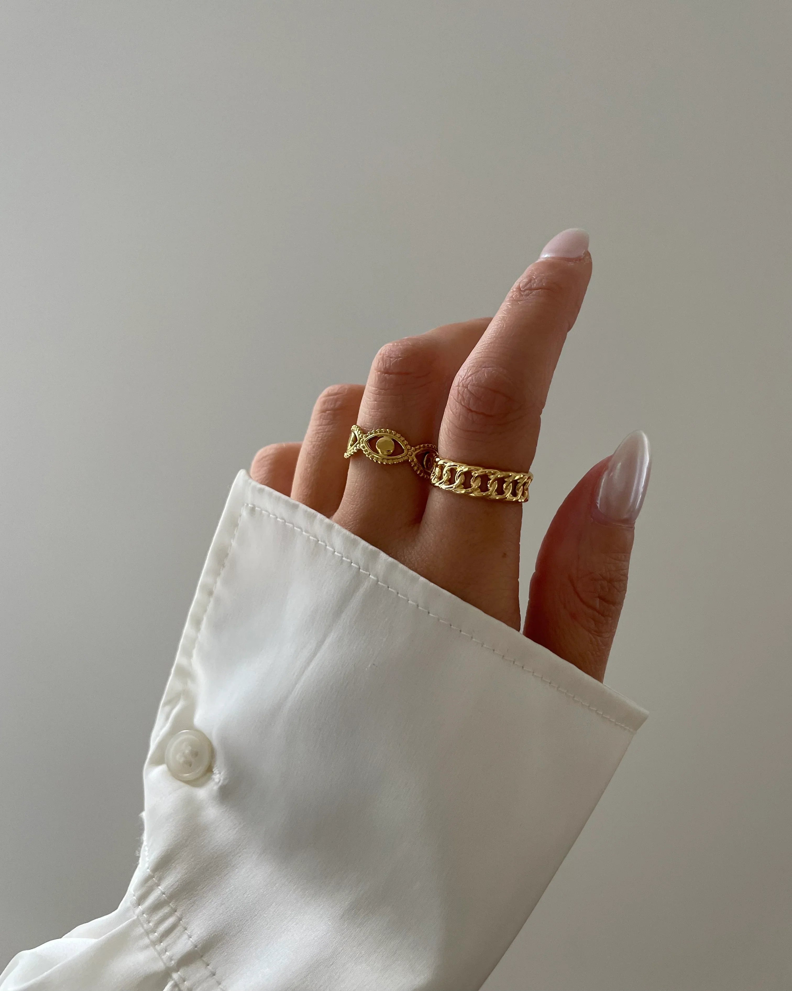 Hand mit zwei goldenen Ringen und weißen langen Nägeln, weiße Hemdmanschette im Hintergrund