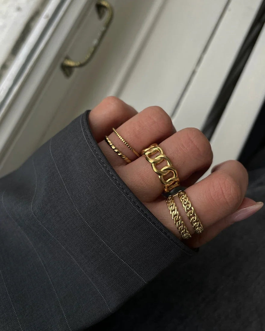 Hand mit fünf goldenen Ringen verschiedener Designs, dunkles langärmliges Oberteil, Nahaufnahme