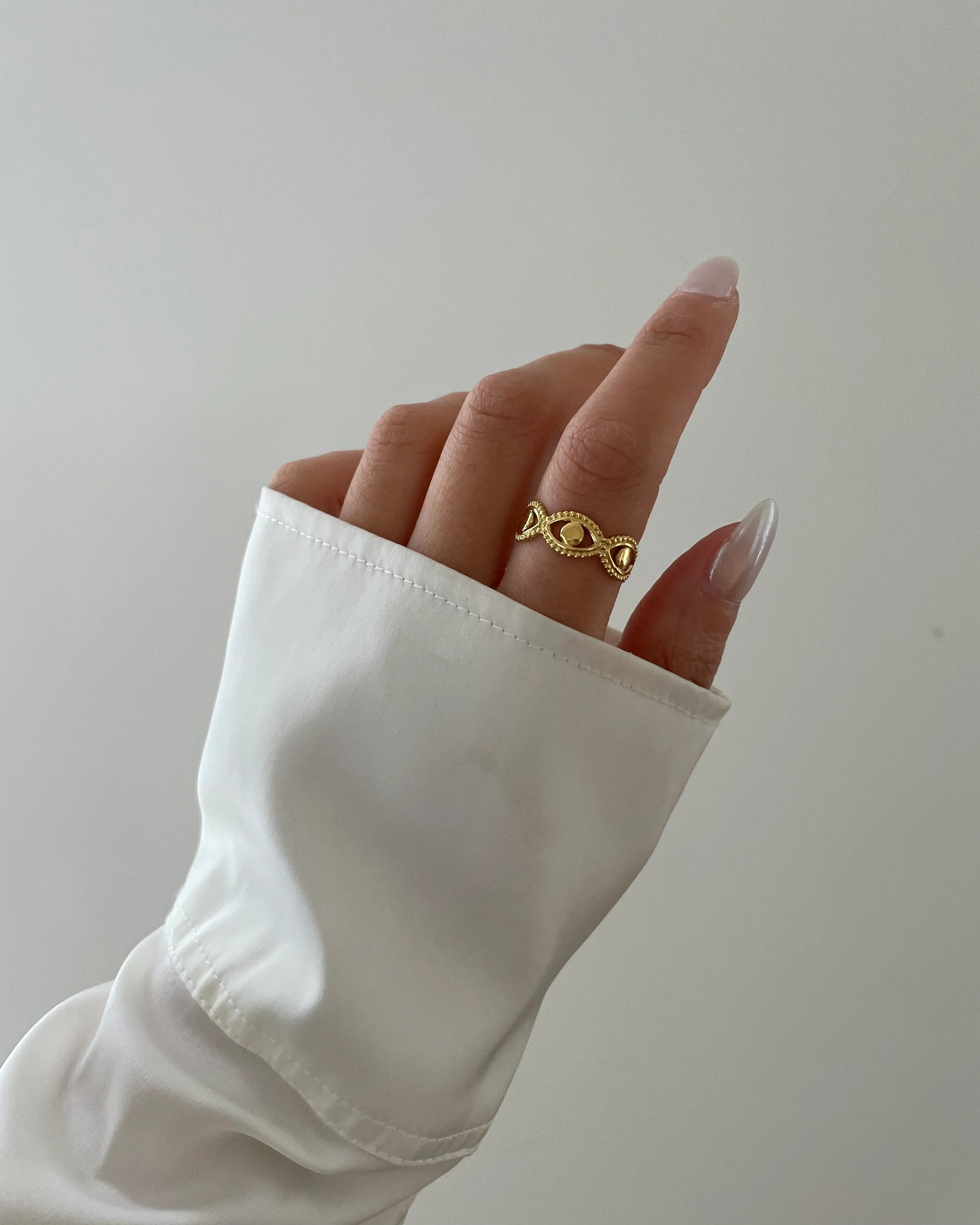Hand mit goldfarbenem, dekorativem Ring und weißem Ärmel vor hellem Hintergrund