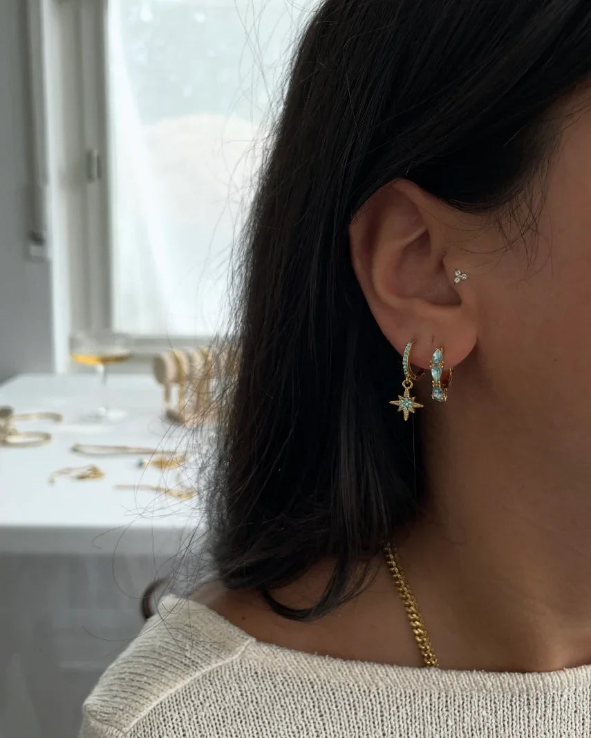 Frau mit goldenen und türkisfarbenen Ohrringen, Sternanhänger, zarter Schmuck in hellem Raum