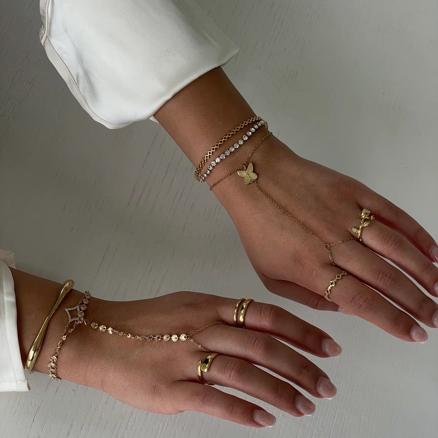 Hände mit goldfarbenem und silberfarbenem Schmuck, darunter Ringe, Armbänder und zarte Ketten mit Schmetterlingsanhänger