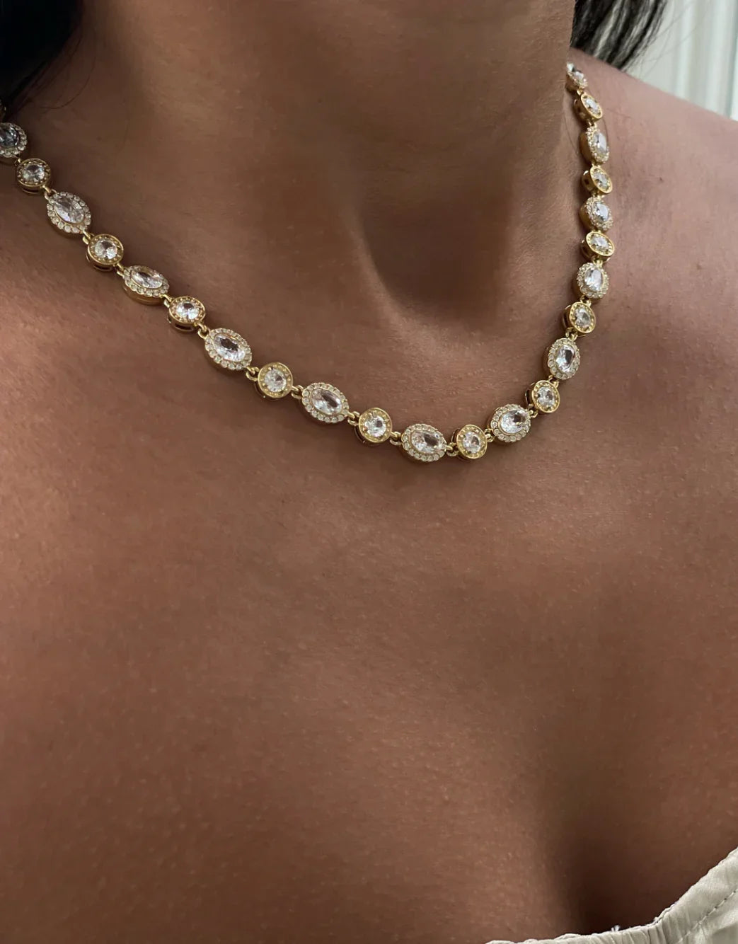 Nahaufnahme einer goldenen Halskette mit ovalen und runden Kristallen auf brauner Haut