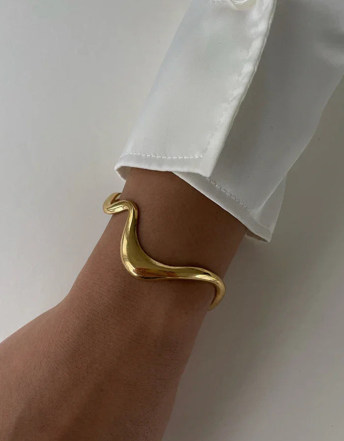 Goldene, geschwungene Armspange aus Metall am Handgelenk mit weißem Hemdsärmel