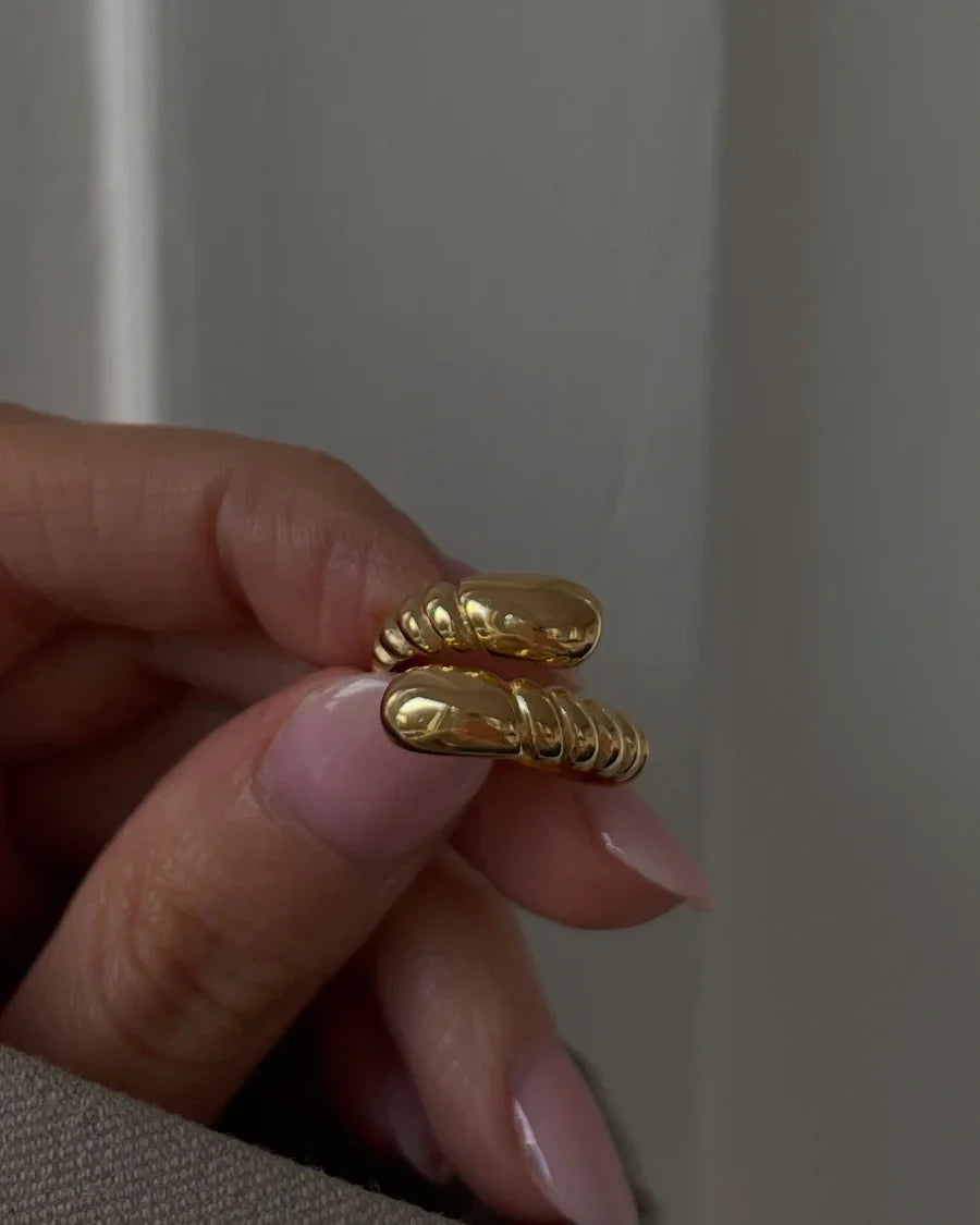 Hand mit langen Nägeln hält goldenen Ring mit glatter und gerippter Oberfläche