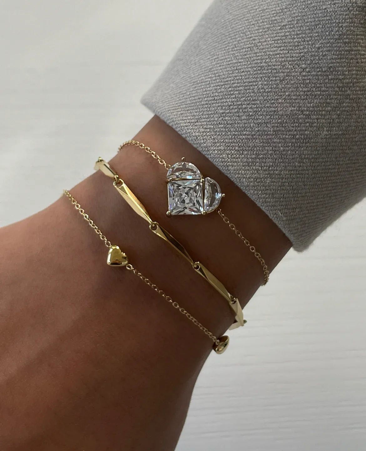 Drei goldene Armbänder am Handgelenk mit funkelndem Herz-Diamant und feinem Schmuck