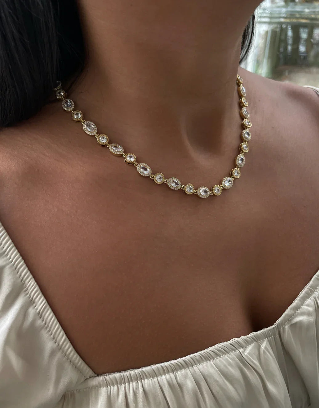 Feine goldene Halskette mit ovalen und runden Kristallen, getragen von Frau im weißen Oberteil