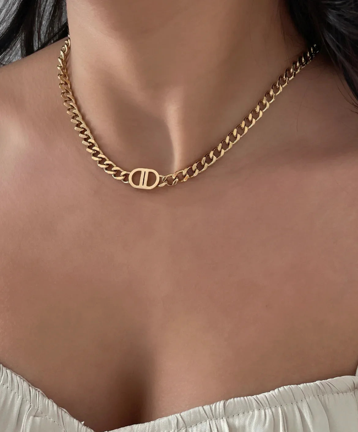 Nahaufnahme einer Frau mit goldenem Kettenhalsband und weißem Oberteil