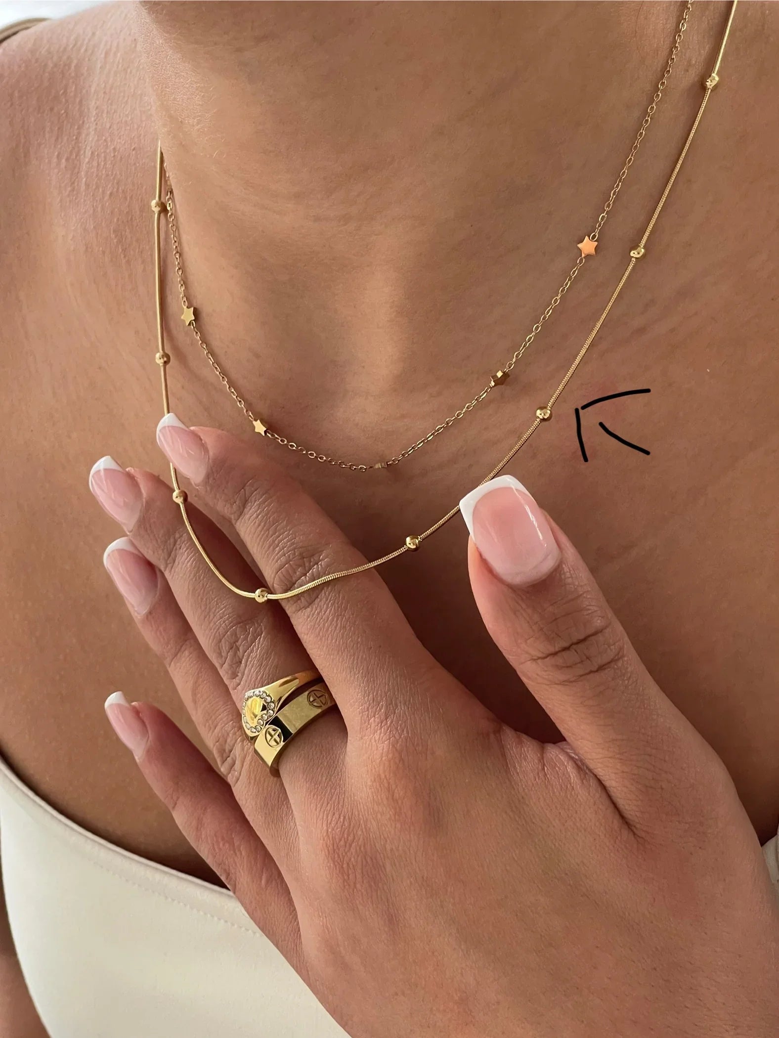 Nahaufnahme goldener Halsketten mit Kugeln und Sternen sowie goldene Ringe an Hand mit French Maniküre