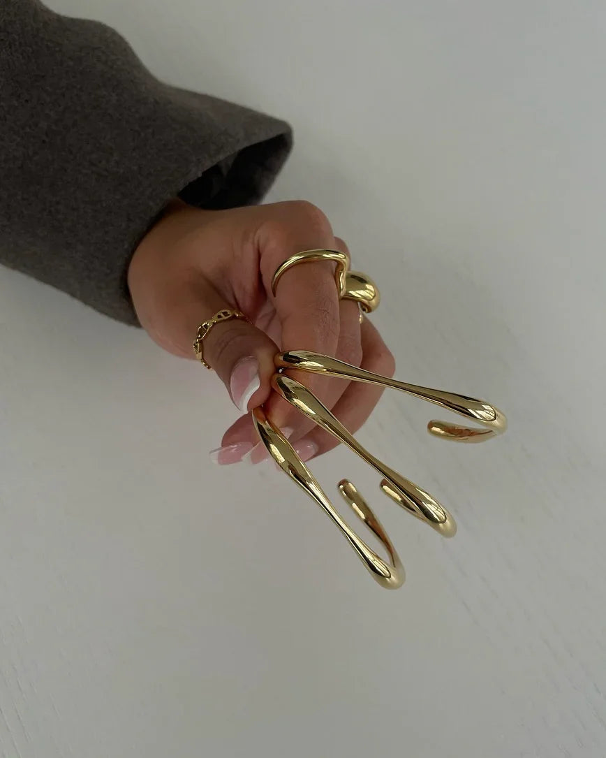 Hand mit langem hellen French-Maniküre-Nagel und mehreren goldfarbenen, organisch geformten Ringen