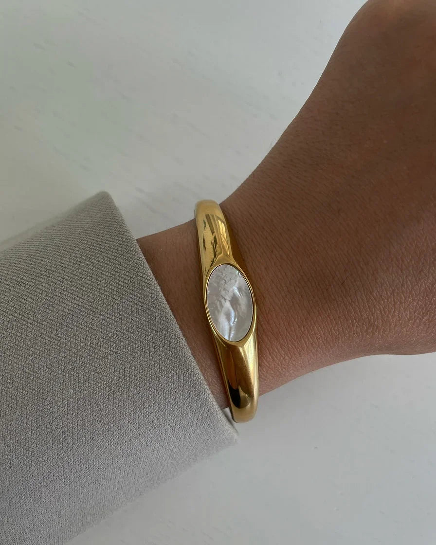 Goldarmband mit großem weißem Perlmutt-Einsatz am Handgelenk, getragen mit grauem Ärmel