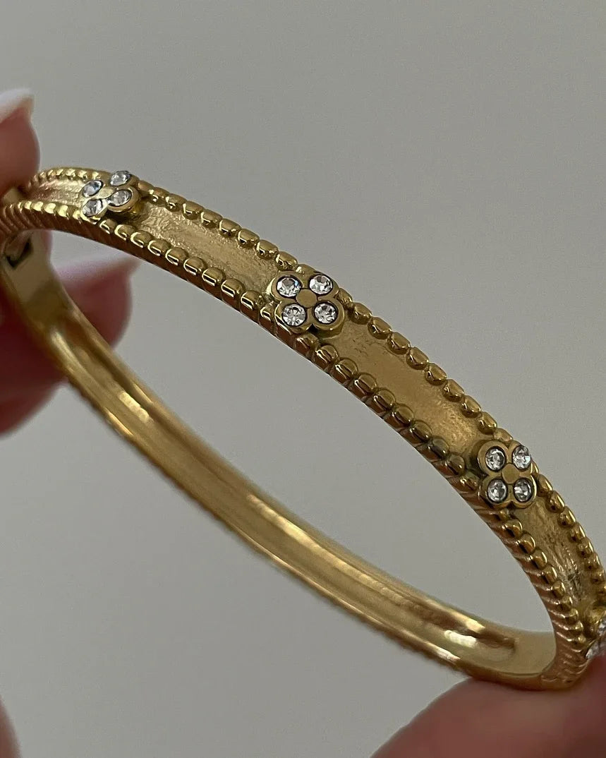 Goldarmband mit dekorativen Strass-Steinen in Blumenmuster, Nahaufnahme vor neutralem Hintergrund