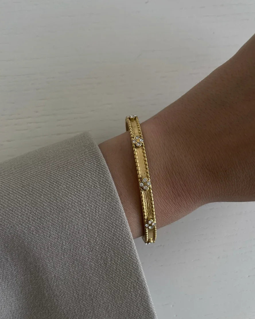 Goldfarbener Armreif mit Diamantbesatz am Handgelenk einer Person mit beigem Mantel