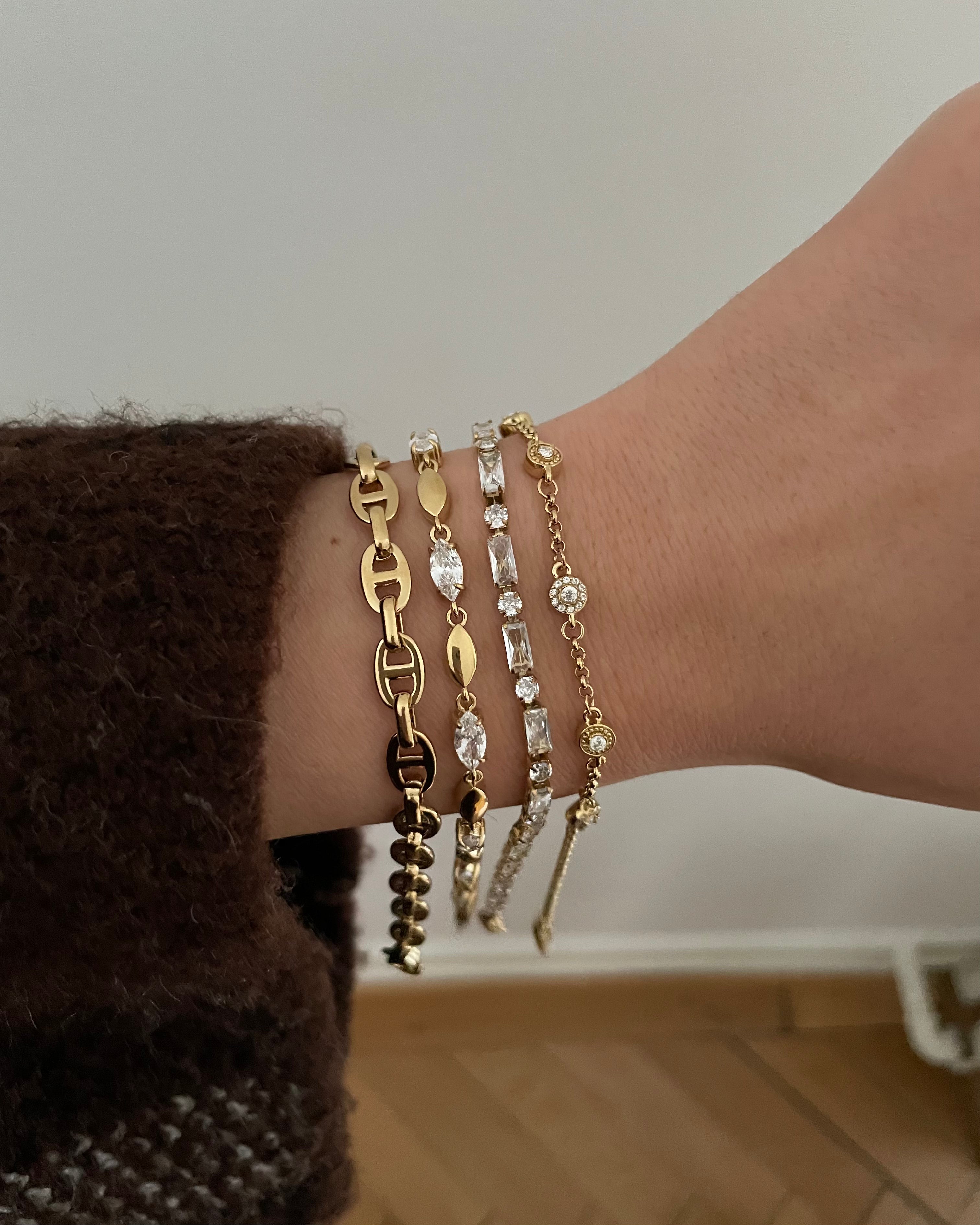 Hand mit vier goldenen Armbändern, darunter Gliederkette und Schmuck mit Zirkonia-Steinen