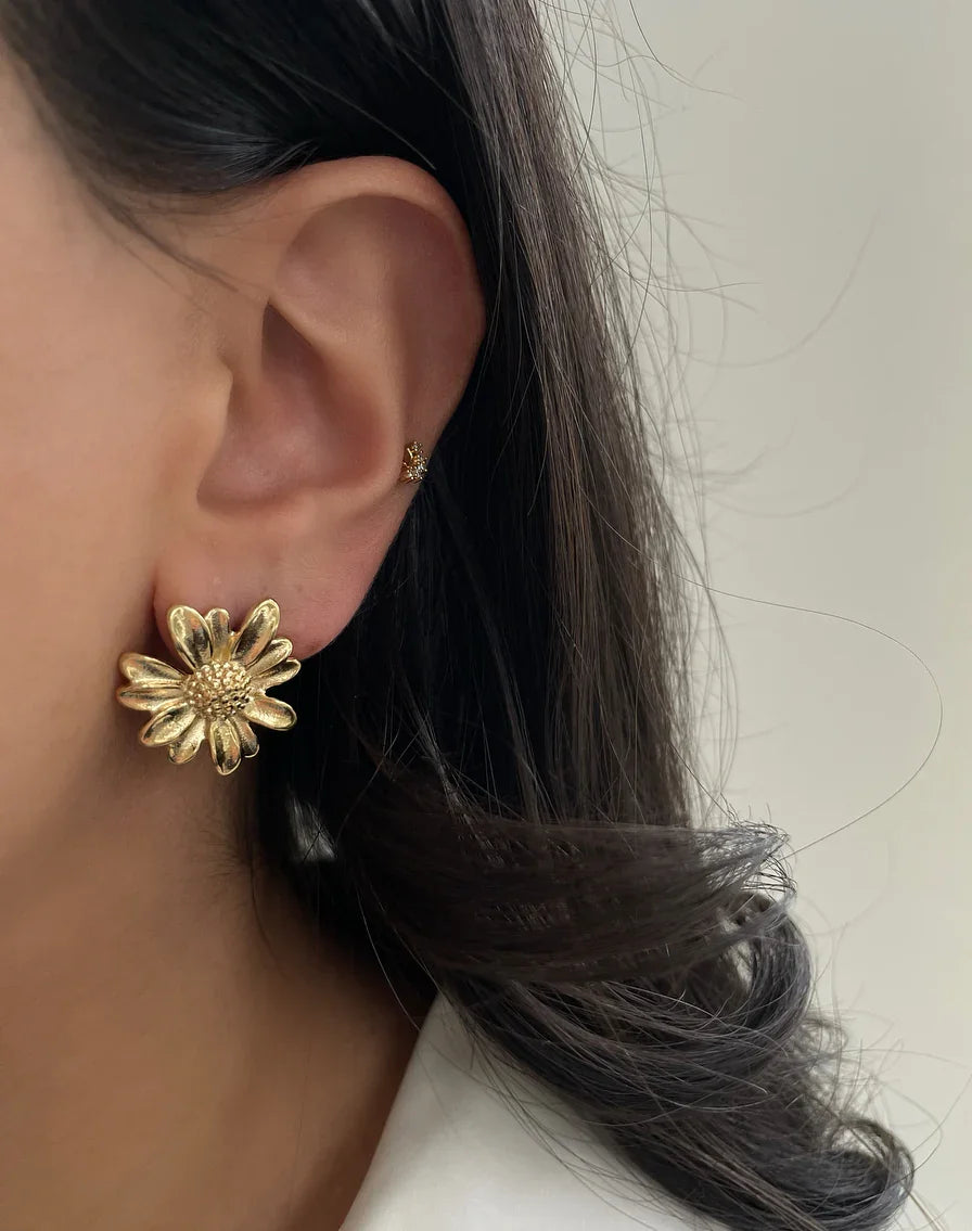 Nahaufnahme eines Ohrs mit goldener Blumen-Ohrring und kleinem steinbesetztem Ohrstecker