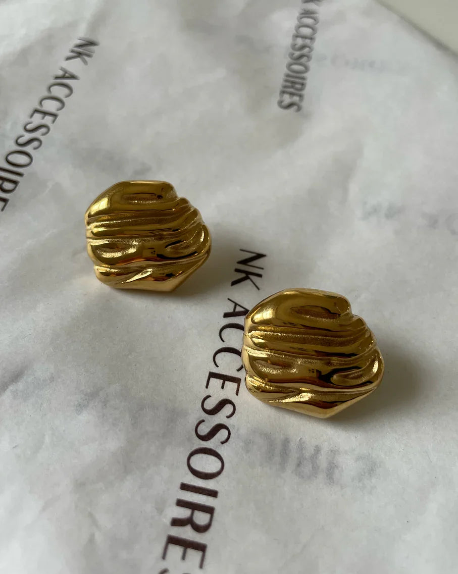 Goldene, strukturierte Ohrstecker auf weißem Papier mit schwarzem NK Accessoires Text