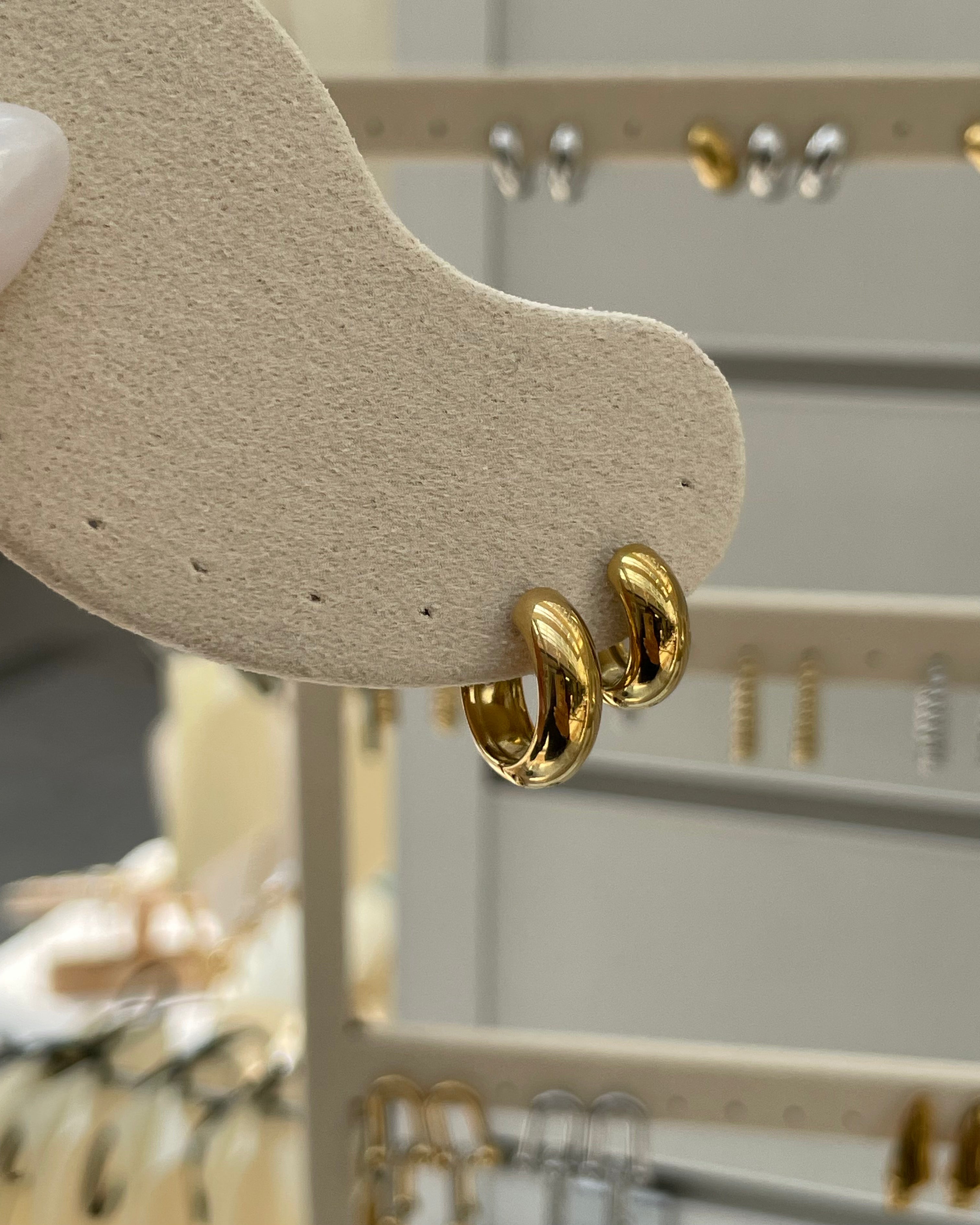 Goldene Creolen-Ohrringe auf beigem Schmuckdisplay im Laden mit weiteren Schmuckstücken im Hintergrund