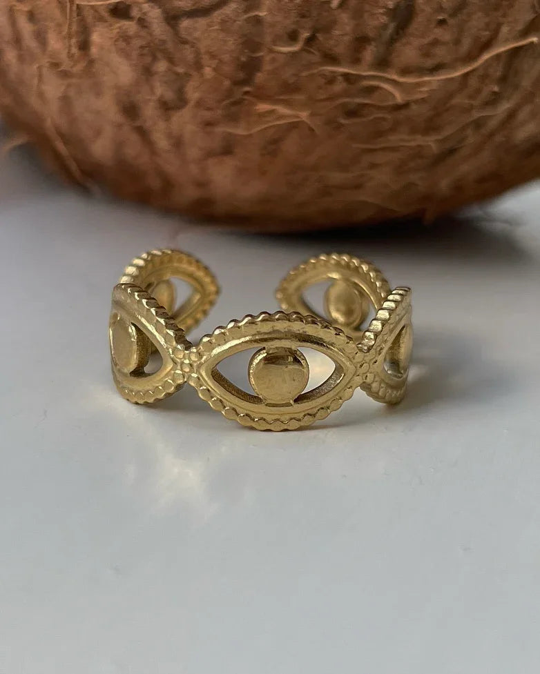 Goldener Ring mit Augendesign auf weißem Hintergrund vor brauner Kokosnuss