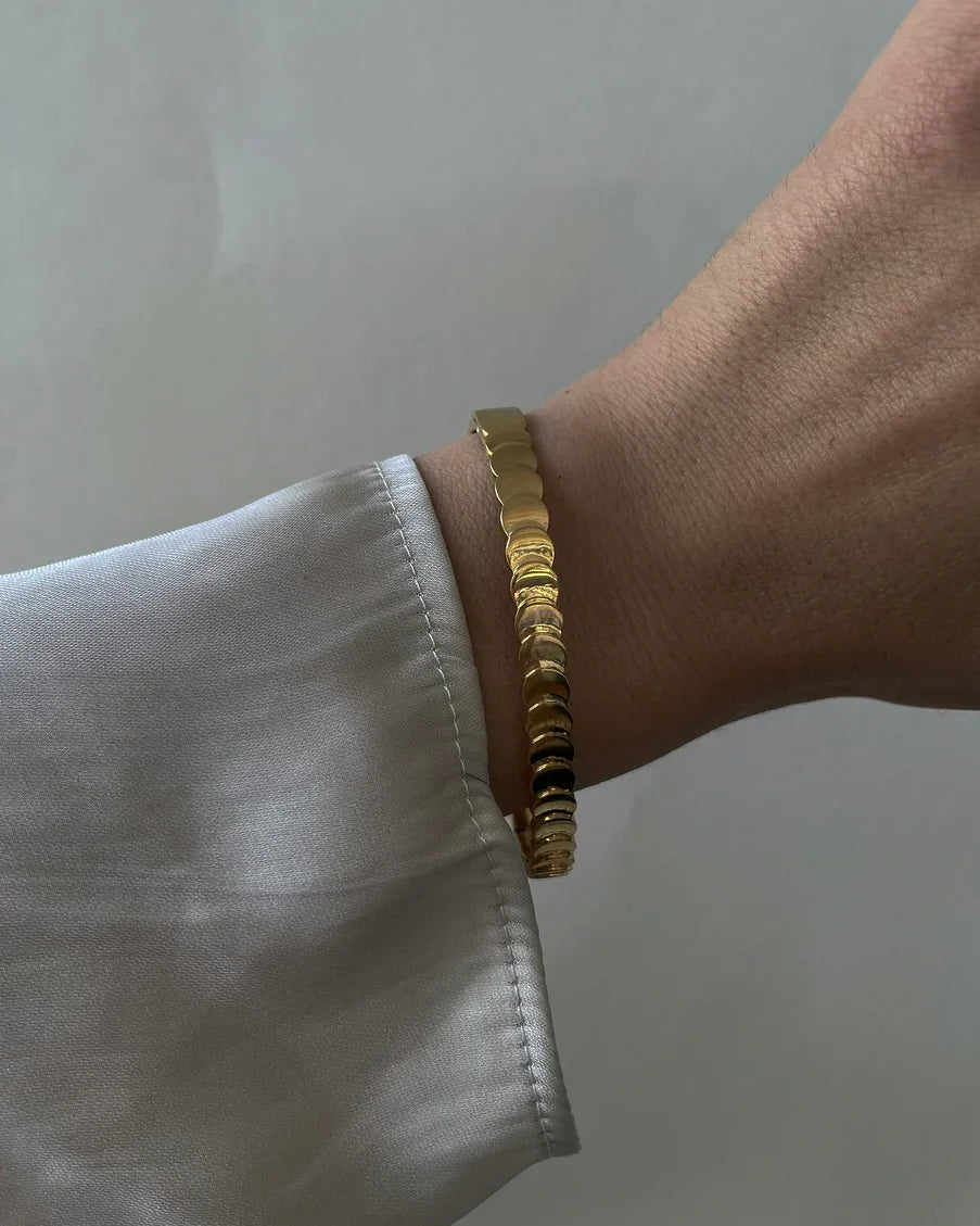 Goldfarbenes, rundes Gliederarmband am Handgelenk über hellgrauem Hemdsärmel