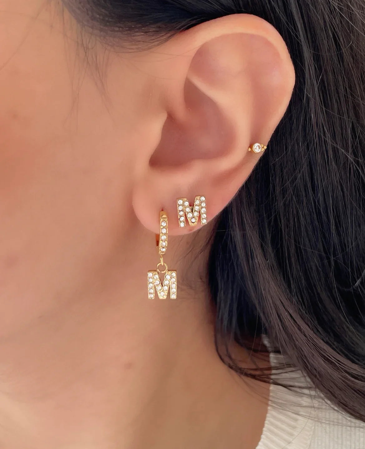 Goldfarbene Ohrstecker mit Buchstabe M und Kristallsteinen an Frauenohr