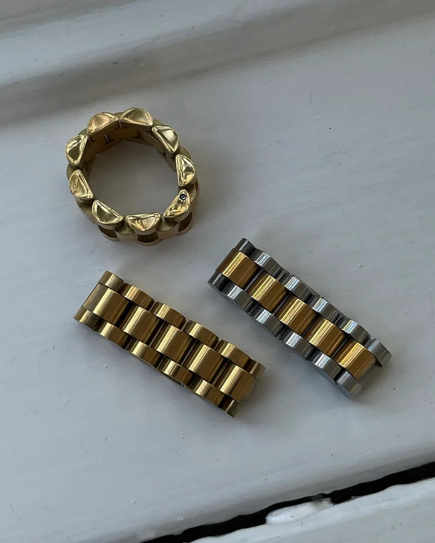 Drei goldfarbene und silberne Uhrarmbandglieder auf weißer Oberfläche, Armband Ersatzteile