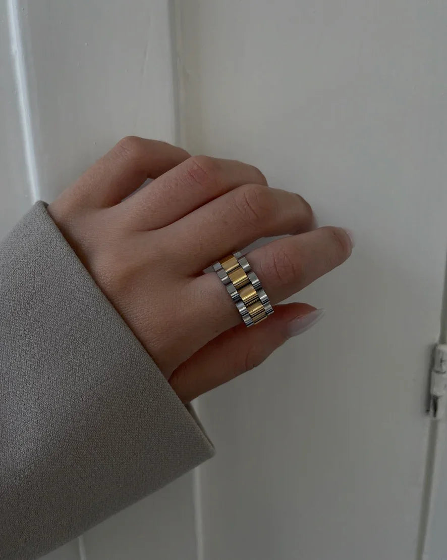 Hand mit zweifarbiger Edelstahl-Goldring im modernen minimalistischen Stil vor hellem Hintergrund