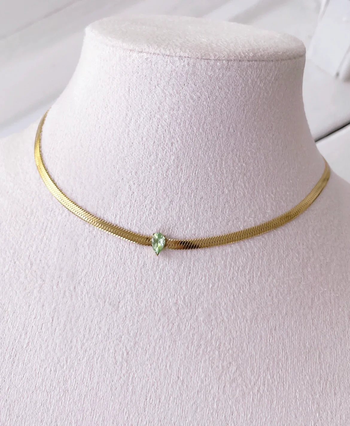 Feine goldene Halskette mit grünem tropfenförmigem Edelstein auf Stoffschmuckständer