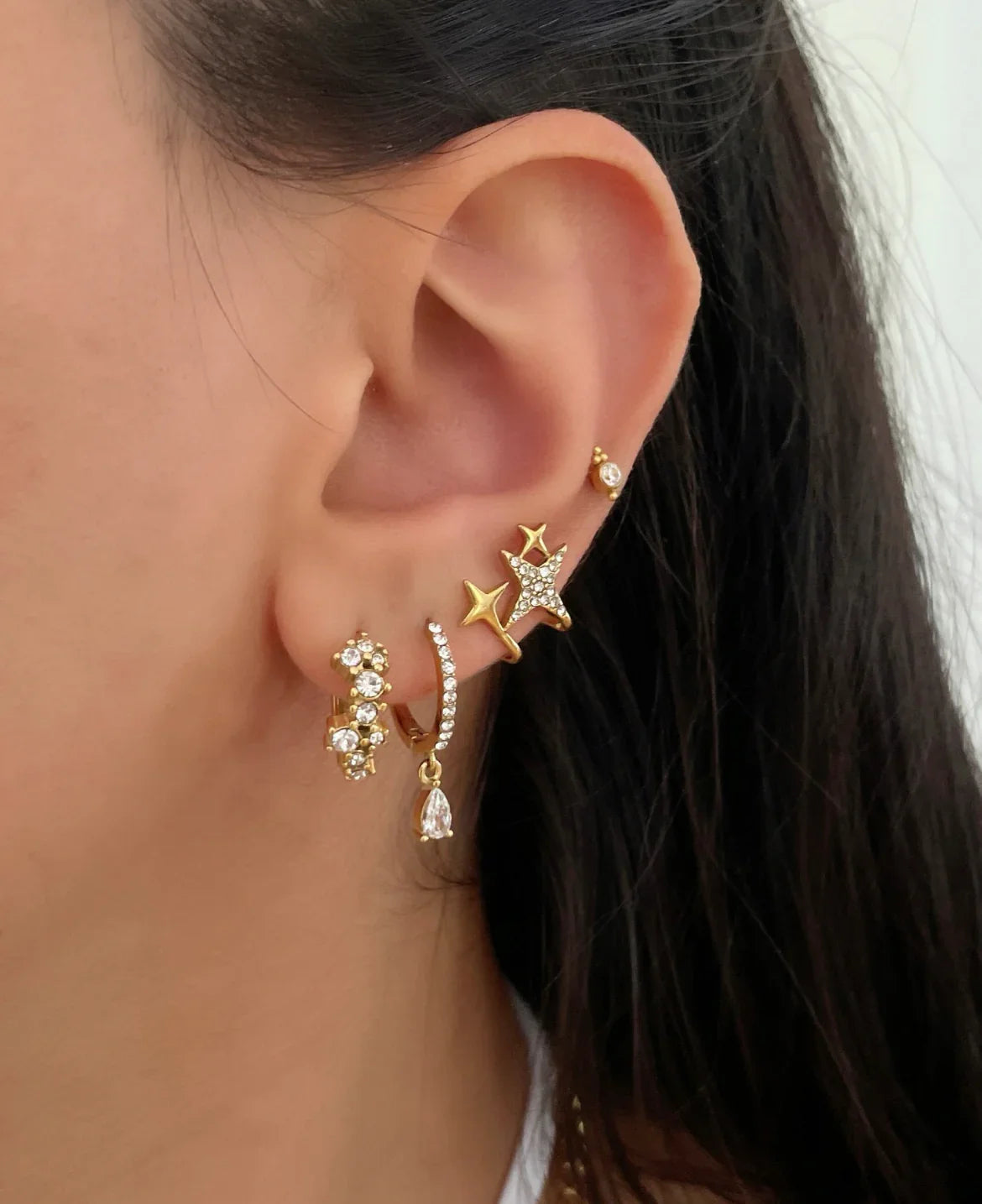 Nahaufnahme eines Ohrs mit fünf goldenen Ohrringen, darunter Sterne und funkelnde Steine