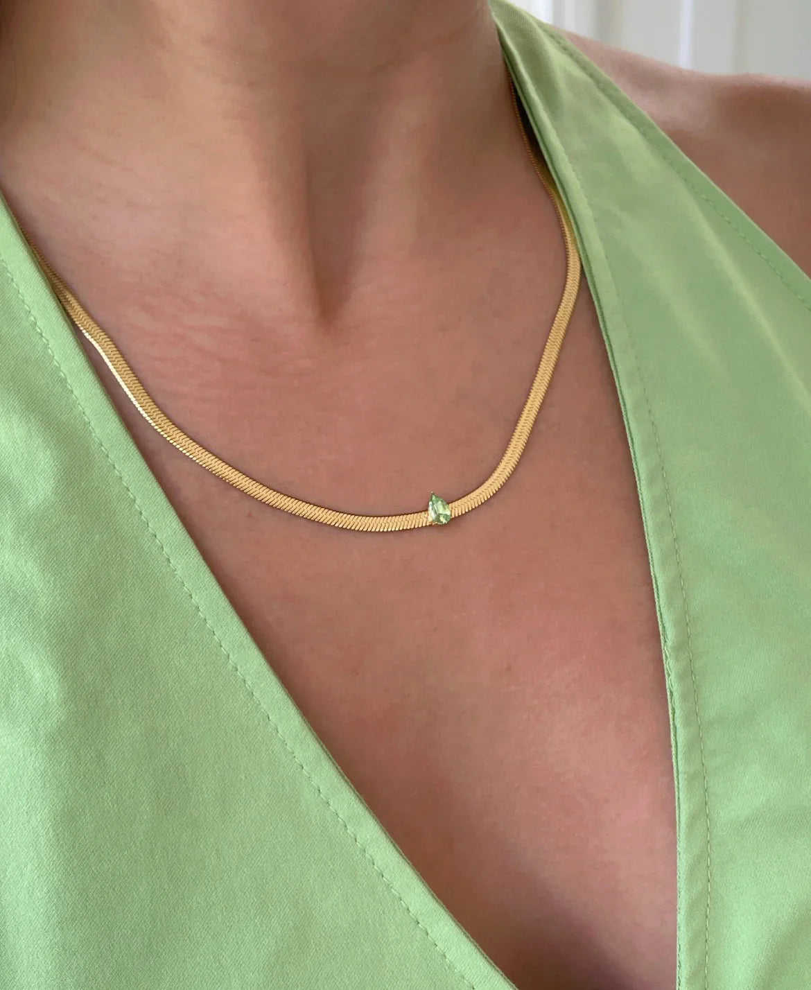 Goldkette mit grünem Tropfenanhänger am Hals einer Person in grünem Oberteil