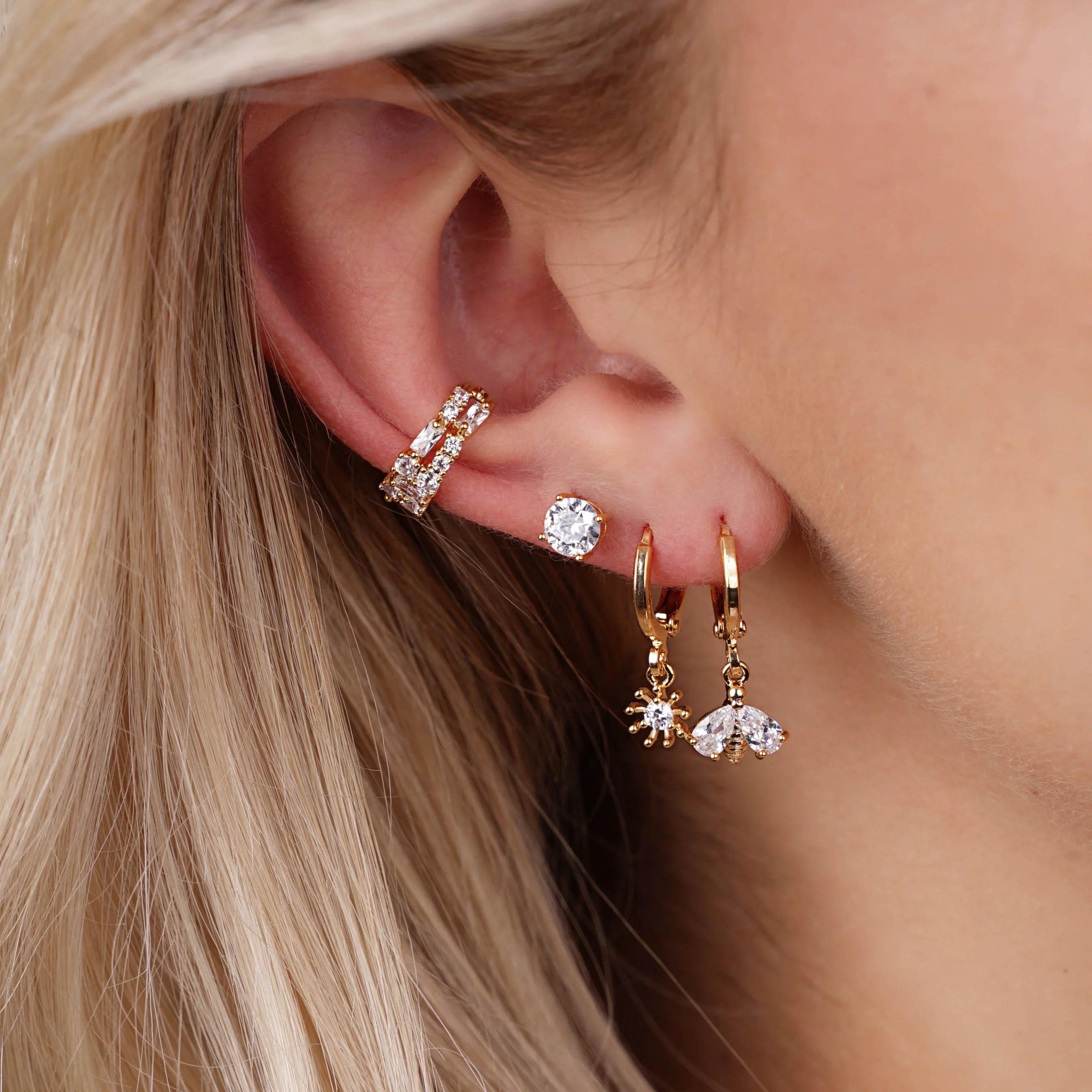 Ohr mit goldenen Ohrringen mit funkelnden Kristallen, darunter Bienen- und Sonnenanhänger