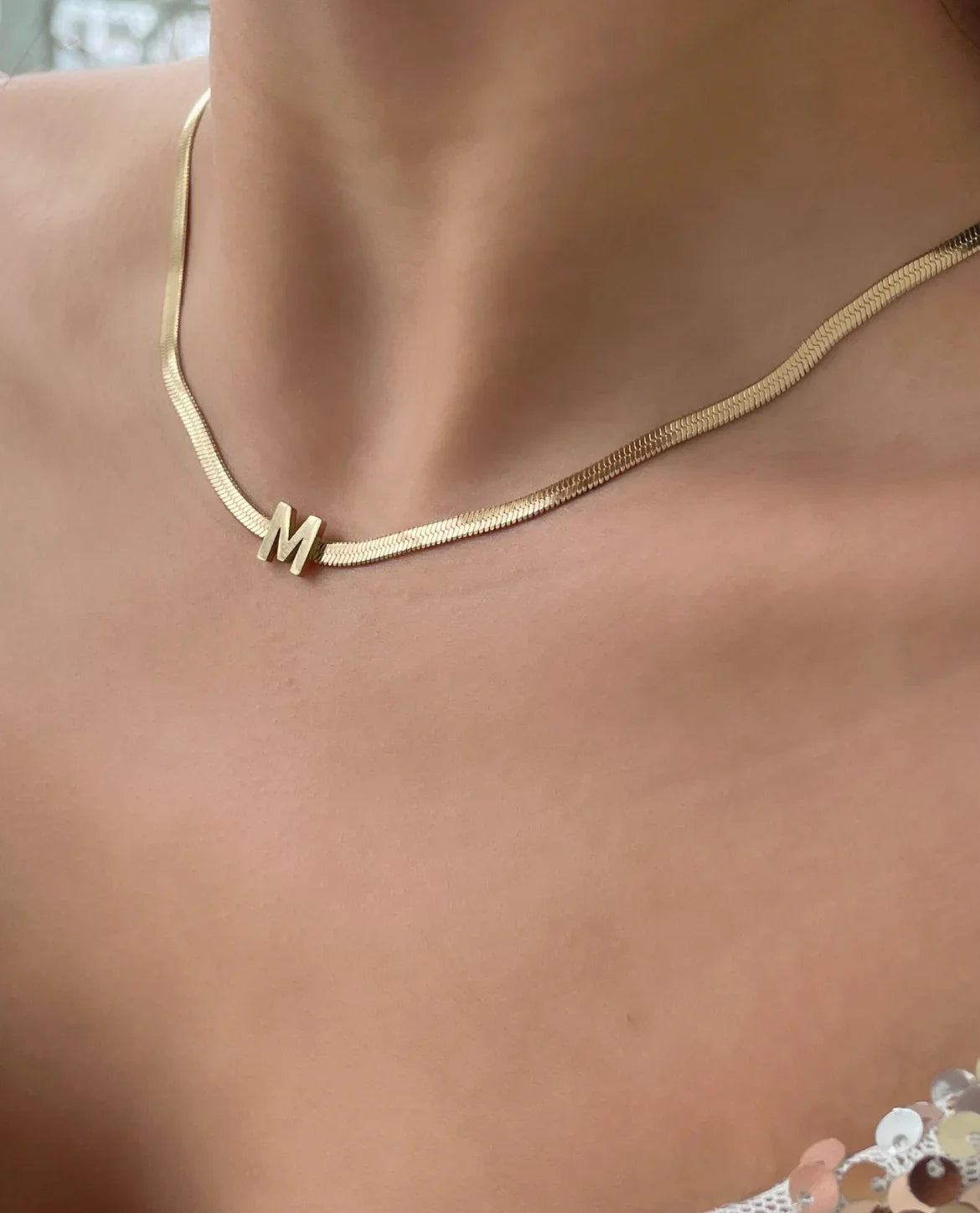 Nahaufnahme einer stilvollen goldenen Halskette mit Buchstabenanhänger M auf heller Haut