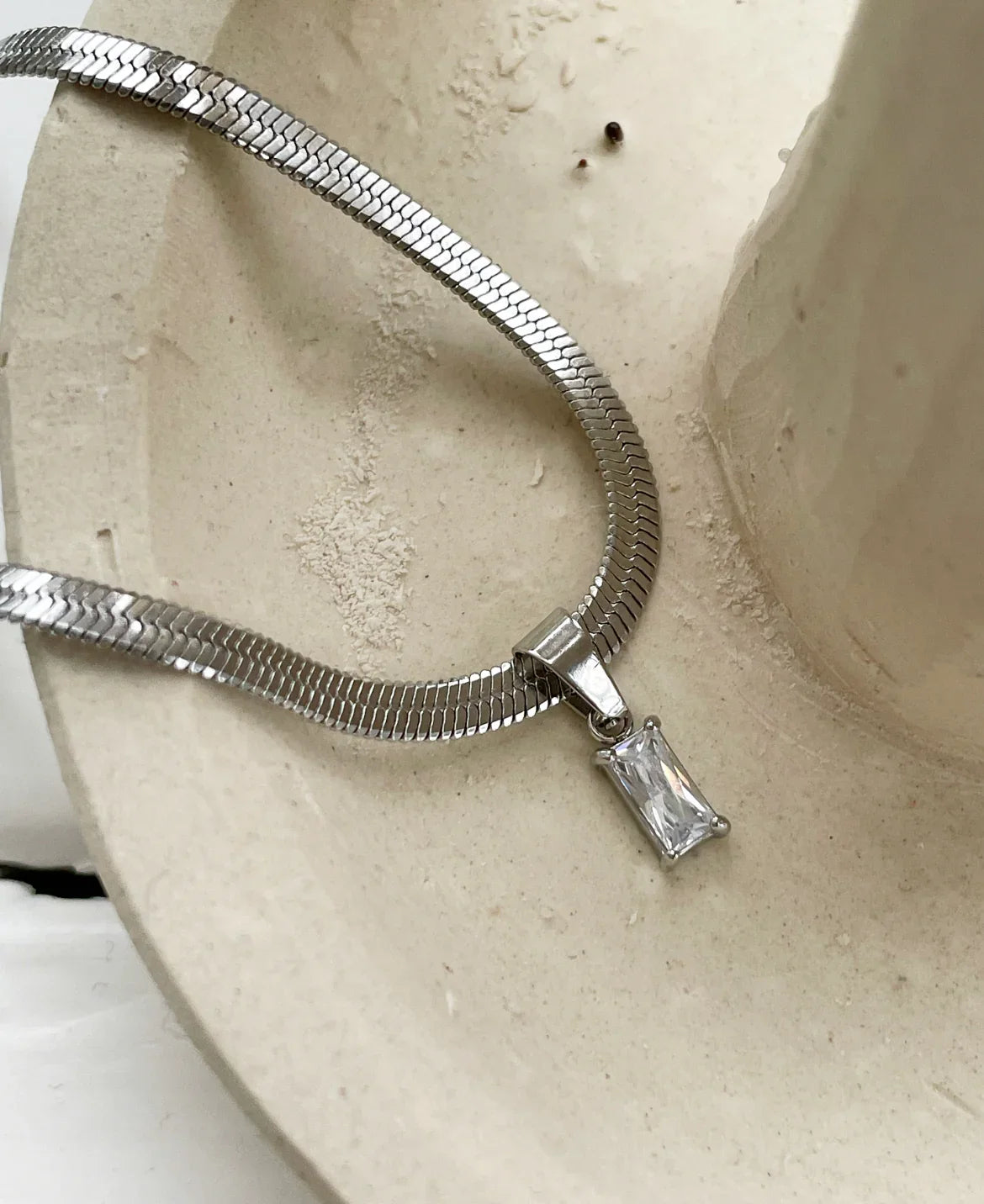 Silberne Halskette mit rechteckigem Kristallanhänger auf beigem Steinuntergrund