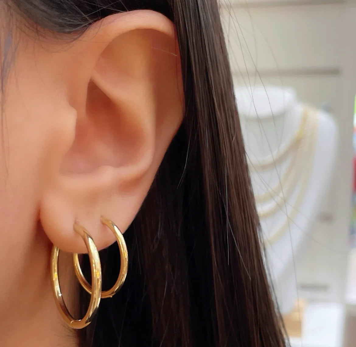 Nahaufnahme Ohr mit zwei goldenen Creolenohrringen und braunen Haaren