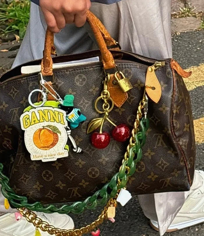Hand hält Louis Vuitton Designer-Tasche mit braunem Monogramm, Schlüsselanhängern und grüner Kettenverzierung